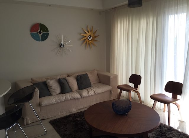 Modern living room with beige sofa, decorative wall clocks, and large window with curtains in Limass.